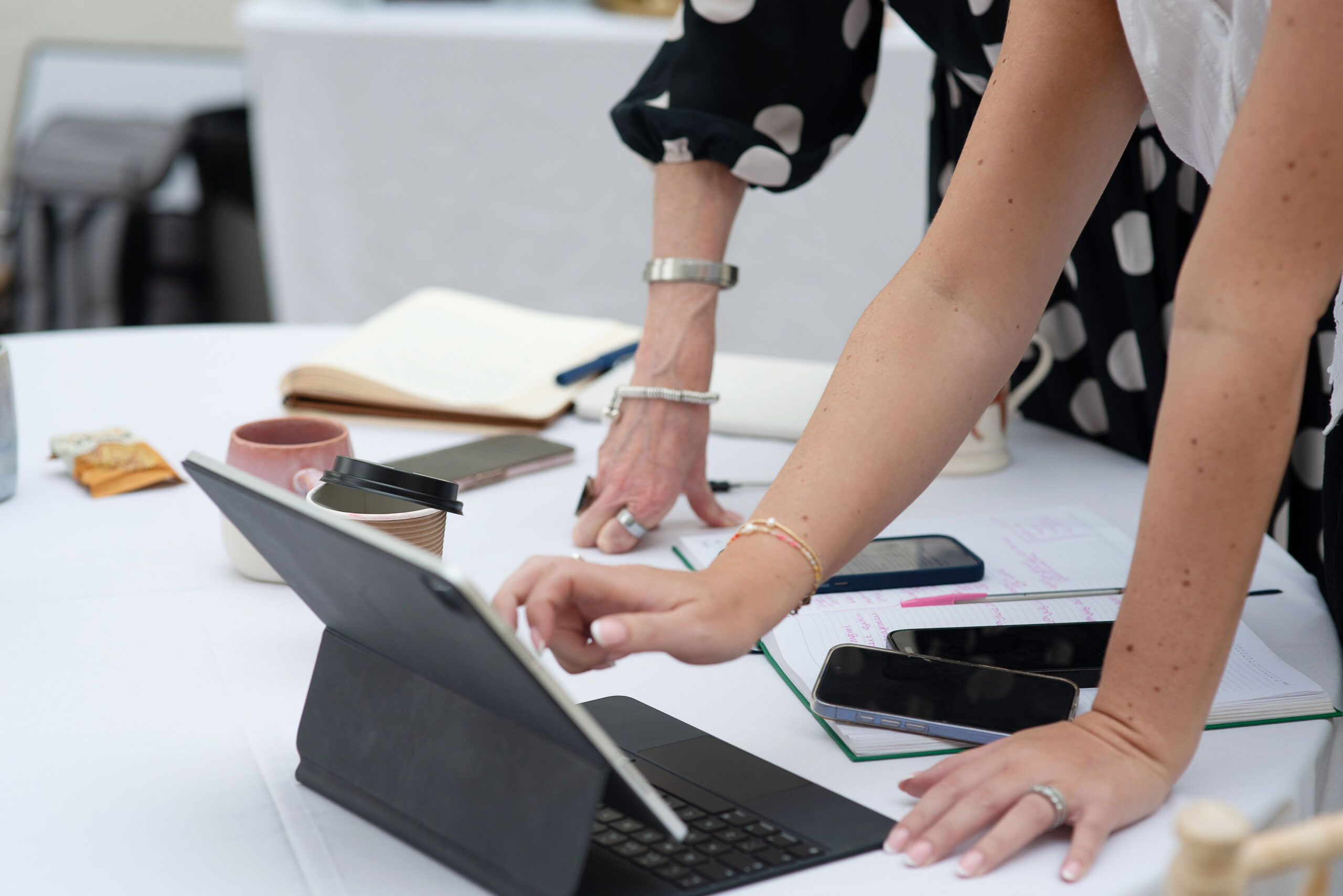 Two people stood up working on their phones and ipad with papers on the table