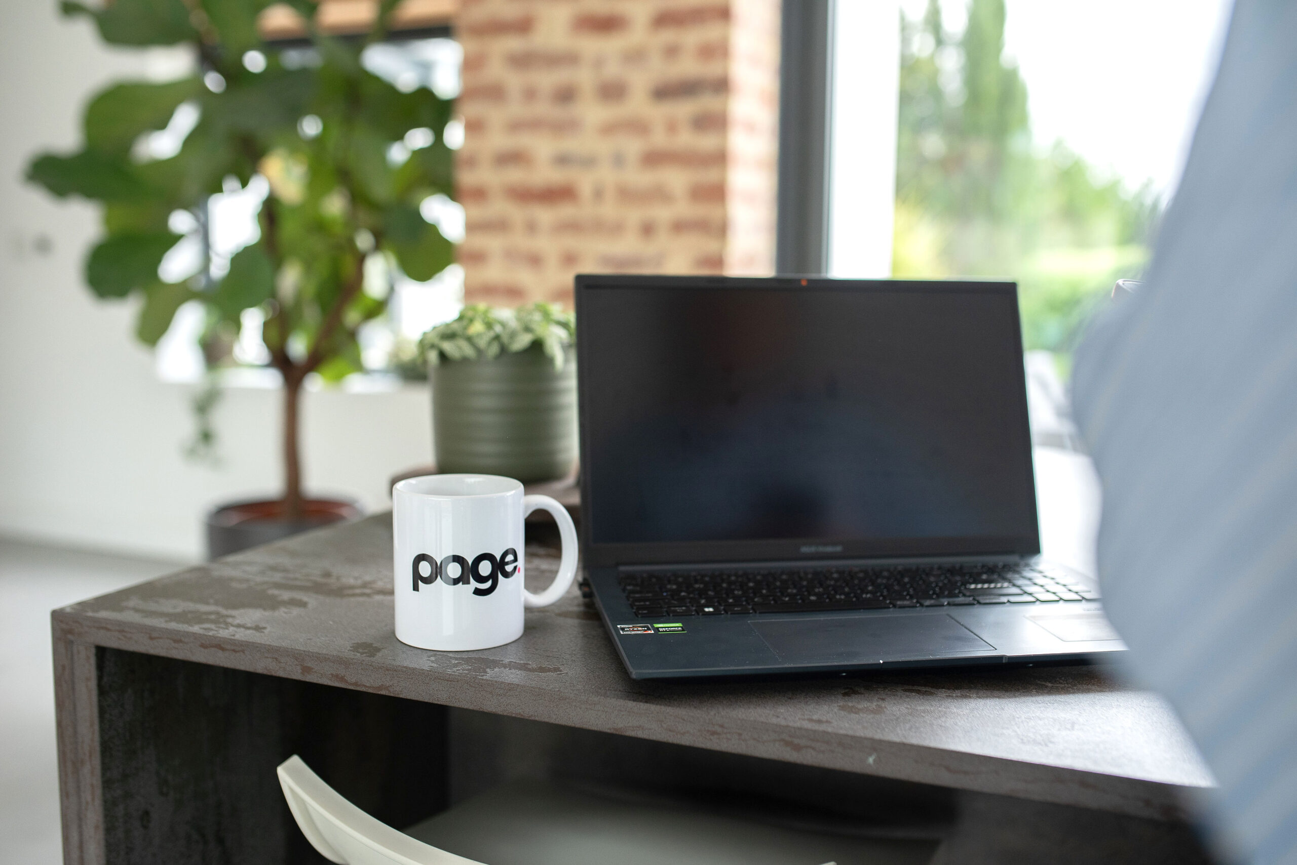 Open computer on table with white mug with 'Page' written on it