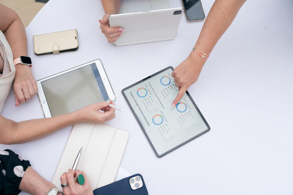 someone pointing at google analytics data on an ipda in the middle of a table, addressing two other people