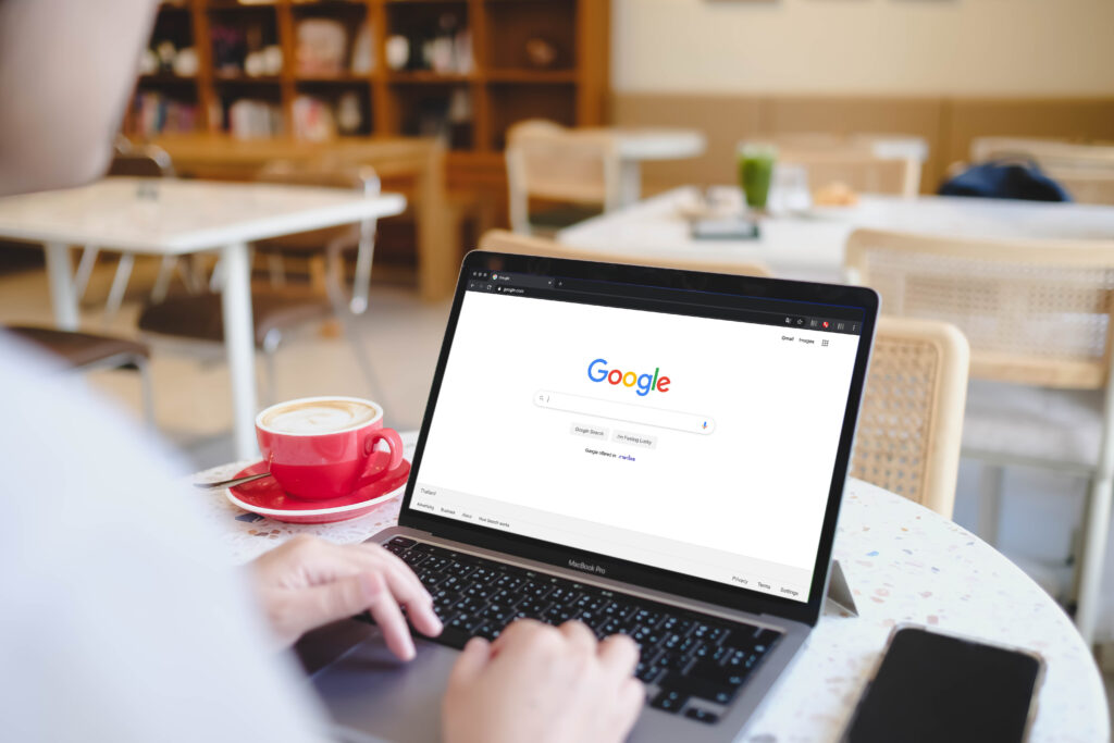 A person using the Google search engine on a MacBook Pro laptop sitting at a terrazzo table in a bright cafe.