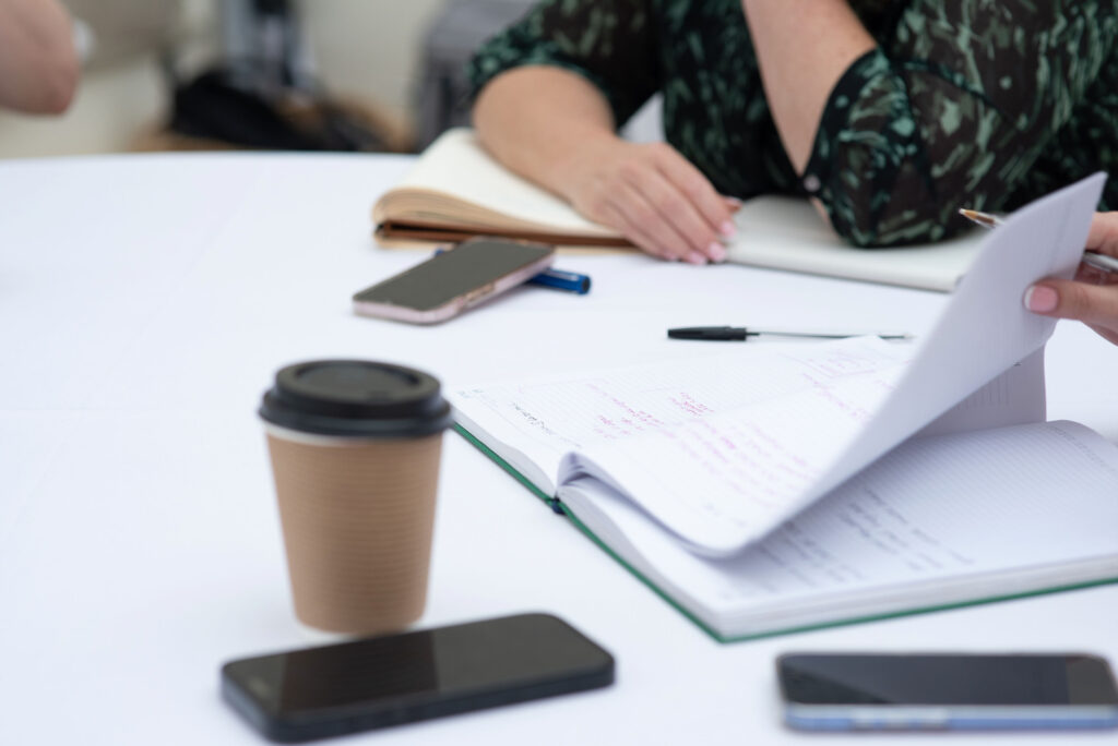 Notebook open on a table during a meeting with coffees and phones in the foreground
