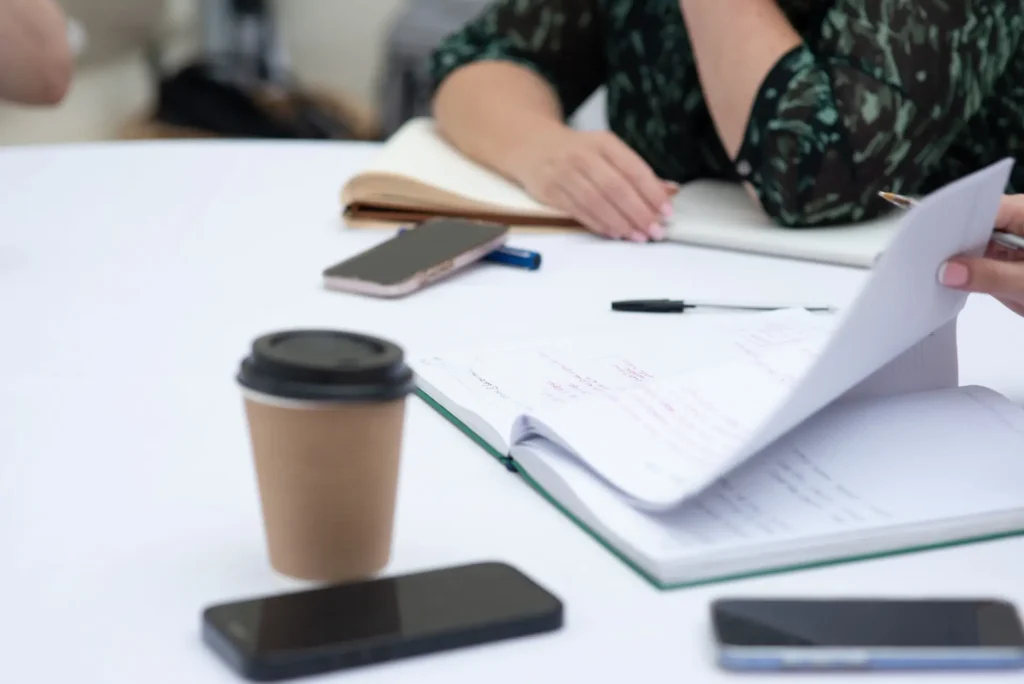 Notebook open on a table during a meeting with coffees and phones in the foreground